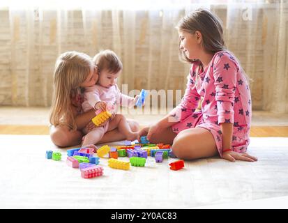 Trois petites filles blonde jouant avec beaucoup de jouets à l'intérieur des blocs colorés. Les soeurs s'amusant avec des capacités et la création d Banque D'Images