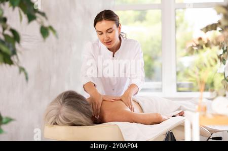 Femme âgée méconnaissable se couche face cachée sur le canapé et profiter de soins spa, massage des épaules Banque D'Images