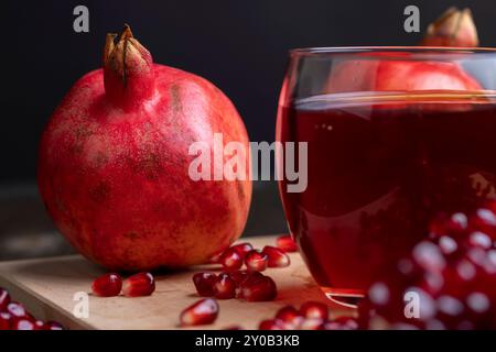 Jus de grenade aigre-douce dans un verre transparent sur la table, à côté de lui se trouvent des grenades mûres rouges avec de gros grains sucrés Banque D'Images