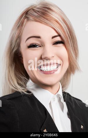 Jeune femme d'affaires blonde sourit largement, montrant des dents blanches parfaites. Elle a un comportement amical et accessible Banque D'Images