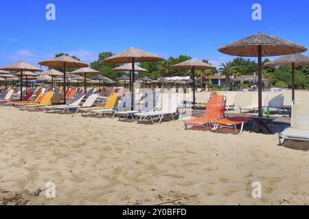 Rangée de parasols en bois et chaise longue au bar de plage de sable, fond de vacances de mer et de ciel bleu, Grèce, Europe Banque D'Images