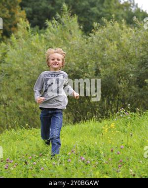 Petit garçon courant dehors sur une prairie. Garçon blond courant à travers un pré Banque D'Images