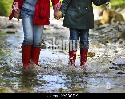 Enfants portant des bottes de pluie sauter dans une rivière de montagne. Close up Banque D'Images