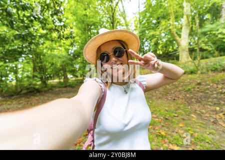 Jeune femme caucasienne qui fait signe de succès tout en prenant un selfie tout en explorant une forêt au printemps Banque D'Images