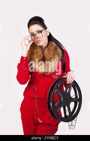 Jeune femme dans un costume de pantalon rouge tient une bobine de film dans sa main Banque D'Images