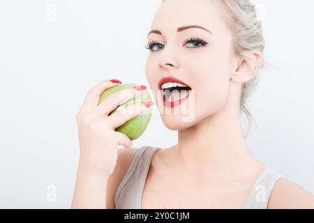 Femme blonde avec rouge à lèvres rouge tient une pomme verte, prête à mordre. Son expression heureuse montre la joie de manger sainement. L'image capture le désir de nutriti Banque D'Images