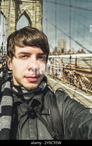 Jeune homme adulte aux cheveux bruns et à la barbe prenant un selfie, regardant l'appareil photo, debout sur le pont de brooklyn New york nyc, etats-unis Banque D'Images