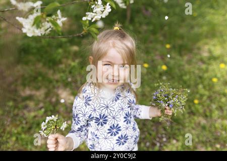 Petite fille avec des fleurs de printemps sur la pelouse verte dans le jardin. Banque D'Images