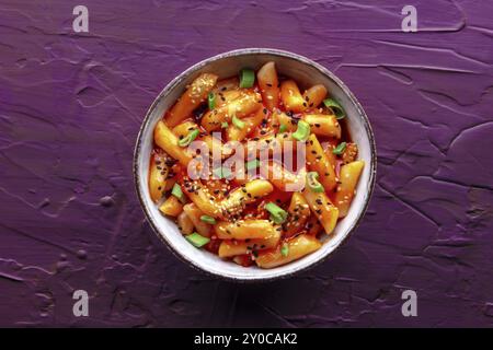 Tteokbokki ou topokki, cuisine de rue coréenne, gâteaux de riz épicés dans la sauce gochujang au poivron rouge, plan posé au plafond sur un fond violet, photogr alimentaire Banque D'Images