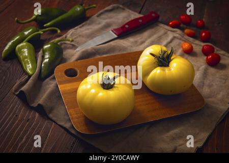 Deux tomates jaunes mûres sur une planche à découper, des poivrons verts épicés et quelques tomates cerises Banque D'Images