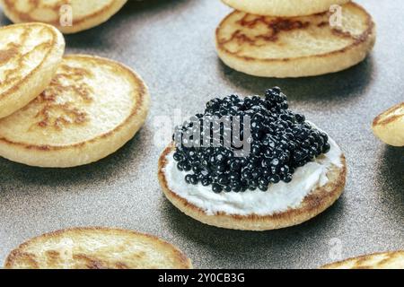 Blinis au caviar noir et fromage à la crème, sur un plat festif, mini crêpes, un apéritif élégant, photographie culinaire Banque D'Images