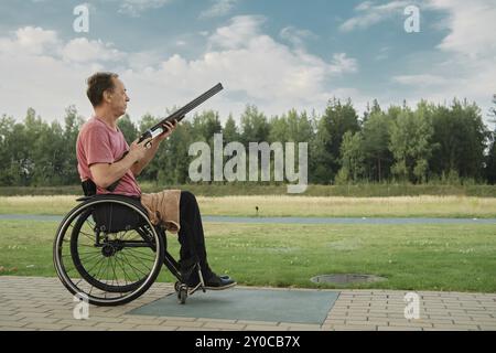 Vue latérale d'un vieil homme déterminé utilisant un fauteuil roulant tenant un fusil à un stand de tir extérieur Banque D'Images