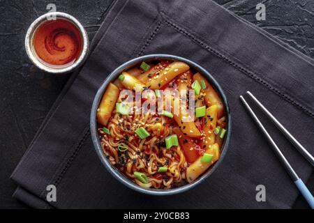 Rabokki, tteokbokki ou topokki avec ramen, cuisine de rue coréenne, gâteaux de riz épicés à la sauce gochujang au poivron rouge, plan de pose à plat au plafond avec un verre et Banque D'Images