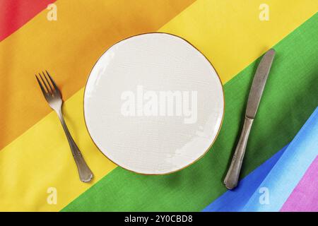 Concept de dîner gay. Un endroit à une table de restaurant LGBT avec une assiette et des couverts, plan de dessus plat sur la texture du drapeau arc-en-ciel Banque D'Images