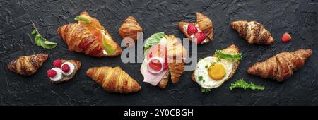 Croissants ensemble sandwich panorama. Différents croissants farcis, plan suspendu plan tiré sur un fond d'ardoise noire. Rouleaux remplis de jambon, saumon, oeuf, Banque D'Images