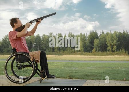 Homme âgé avec les jambes paralysées en fauteuil roulant visant un fusil de chasse à double canon sur un stand de tir extérieur Banque D'Images