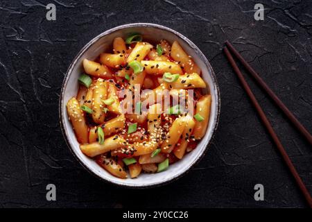 Tteokbokki ou topokki, cuisine de rue coréenne, gâteaux de riz épicés à la sauce gochujang au poivron rouge, tiré du haut avec des baguettes sur un fond noir, Fo Banque D'Images