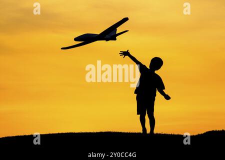 Un jeune garçon vole un avion jouet pendant un coucher de soleil orange vif Banque D'Images