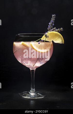 Cocktail avec fruits frais et fleurs. Gin et boisson tonique avec de la glace à une fête, sur un fond noir. Alcool avec lavande et citron Banque D'Images