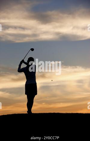 Une silhouette d'une femme golfeuse au coucher du soleil balançant le club de golf Banque D'Images