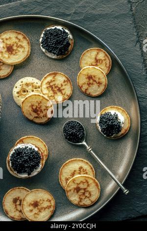 Blinis au caviar noir et au fromage à la crème, photographiés d'en haut, mini crêpes, un apéritif élégant, photographie culinaire Banque D'Images