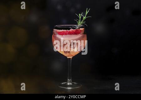 Cocktail de fantaisie avec des fruits frais. Gin et boisson tonique avec de la glace à une fête, sur un fond noir. Alcool avec grapefuit rose et romarin, image tonique Banque D'Images