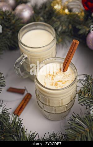 Une photo conceptuelle en gros plan de deux verres de lait de poule avec des bâtonnets de cannelle à l'intérieur d'un récif de noël Banque D'Images