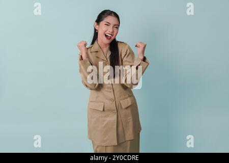 Femme employée du gouvernement indonésien excitée portant un uniforme kaki posant avec une expression heureuse et réussie. PNS concept de fonctionnaire. Banque D'Images