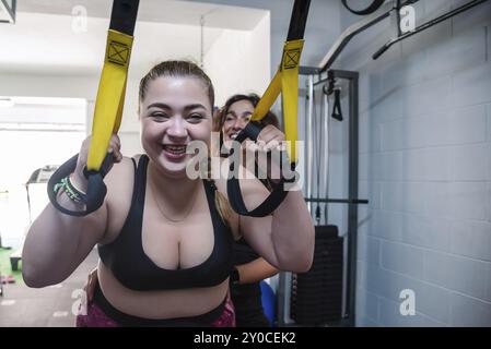 Jeune fille en surpoids qui s'entraîne dans un gymnase et supervisée par son entraîneur. Suspendu à une corde. Elle est très motivée et engagée Banque D'Images