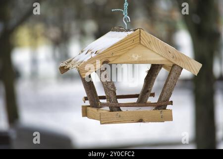 Mangeoire à oiseaux en bois, en forme de petite maison, suspendue à une ficelle dans un environnement enneigé, le fond est flou, contenant des arbres couverts de neige Banque D'Images