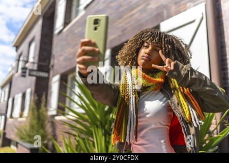 Beauté femme latine geste victoire tout en prenant un selfie debout à côté d'une maison Banque D'Images