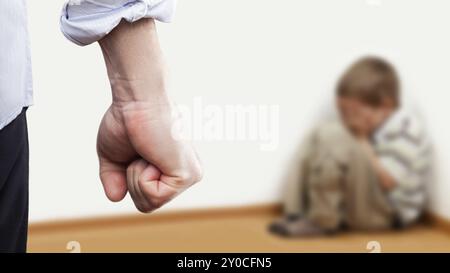 Concept de violence familiale et d'agression, furieux homme en colère leva le poing de punition pour enfant garçon effrayé ou terrifié assis au coin du mur Banque D'Images