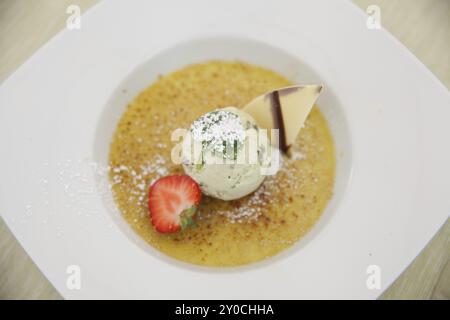 Assiette avec une boule de glace, une fraise, un morceau de chocolat à la sauce jaune Banque D'Images