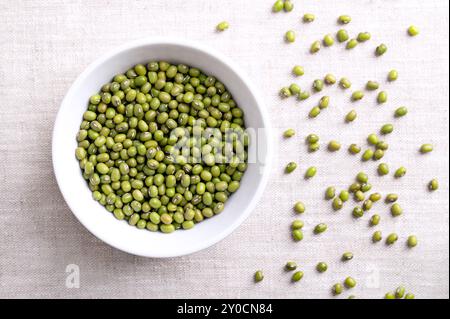 Haricots mungo, gramme vert dans un bol blanc sur tissu de lin. Graines séchées de Vigna radiata, un membre de la famille des légumineuses Fabaceae. Banque D'Images