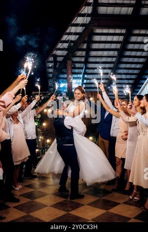 feu froid des bougies de gâteau et des feux d'artifice dans les mains des gens autour des jeunes mariés Banque D'Images