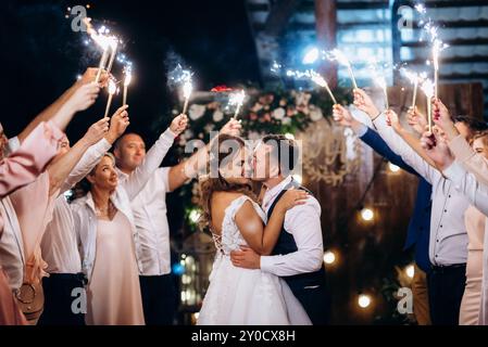 feu froid des bougies de gâteau et des feux d'artifice dans les mains des gens autour des jeunes mariés Banque D'Images