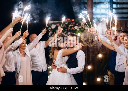 feu froid des bougies de gâteau et des feux d'artifice dans les mains des gens autour des jeunes mariés Banque D'Images