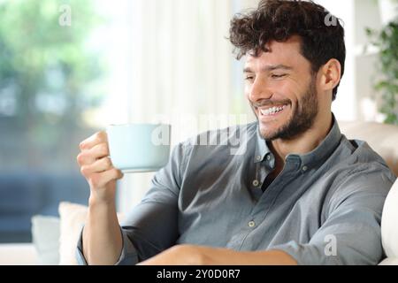 Homme heureux regardant une tasse de café assis sur un canapé à la maison Banque D'Images