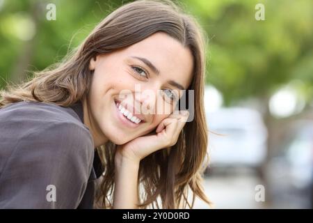 Femme heureuse avec le sourire parfait et les dents regarde la caméra assis dans un parc Banque D'Images