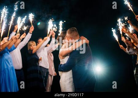 feu froid des bougies de gâteau et des feux d'artifice dans les mains des gens autour des jeunes mariés Banque D'Images