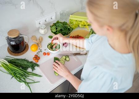 Une femme est vue d'en haut, coupant un concombre dans un cadre de légumes frais Banque D'Images