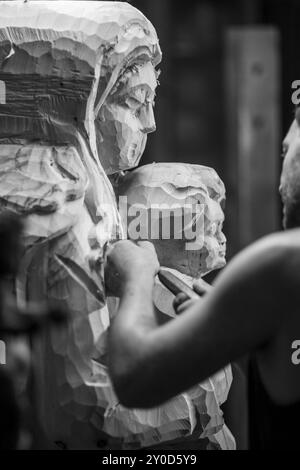 Gros plan des mains d'un artiste qui travaille sur une statue en bois, en utilisant un ciseau pour façonner le bois avec précision. L'image en noir et blanc capture le Banque D'Images