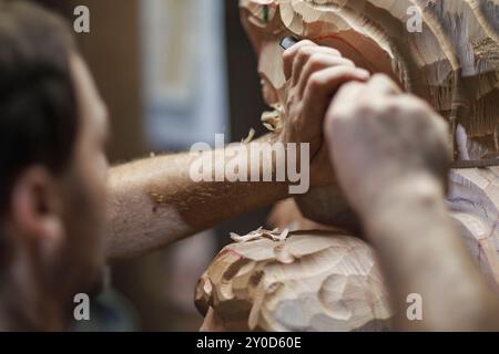 Menuisier habile sculpte une sculpture en bois dans son atelier avec précision et passion, entouré d’outils et de sciure de bois Banque D'Images