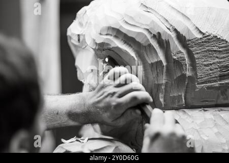 Gros plan des mains d'un artiste qui travaille sur une statue en bois, en utilisant un ciseau pour façonner le bois avec précision. L'image en noir et blanc capture le Banque D'Images