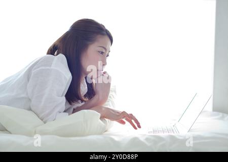 Une femme utilisant un ordinateur couchée sur un lit Banque D'Images
