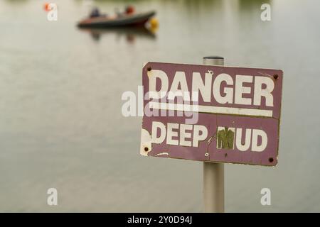 Signer : Danger, boue profonde, avec un bateau dans l'arrière-plan flou, vu à Topsham, Devon, UK Banque D'Images