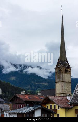 La belle flèche d'une église à Bischofshofen, Autriche dans les superbes Alpes autrichiennes, avec des nuages bas suspendus sur les forêts de montagne derrière. Banque D'Images