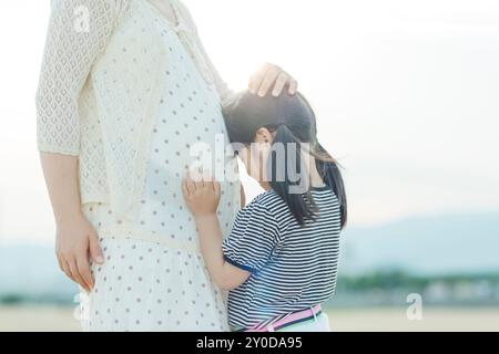 Une fille pressant son visage contre le ventre enceinte de sa mère Banque D'Images