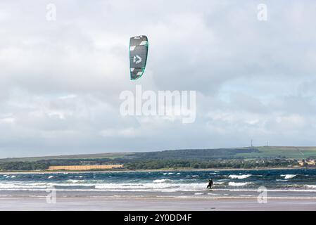 Dunnet, Écosse, Royaume-Uni - 30 août 2024 : kite surf homme avec un cerf-volant dans le ciel à bord dans les vagues de l'équitation de mer dans Dunnet Bay, l'un des embellisses de l'Écosse Banque D'Images