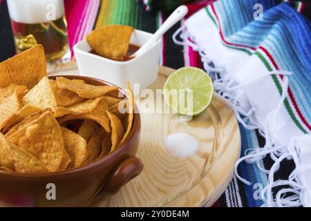 Nachos chips dans un bol sur une planche à découper avec la sauce tomate et le sel de chaux de la bière avec l'arrière-plan poncho Banque D'Images